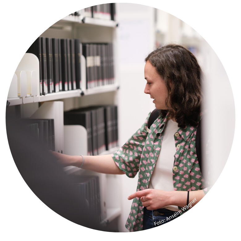 Studentin beim Betrachten von Büchern in einem Regal der Universitätsbibliothek Marburg
